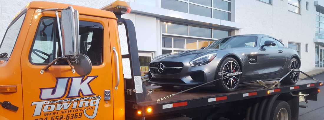 JK Towing's flatbed tow truck carrying a luxury car that is carefully tied down with synthetic straps around its tires
