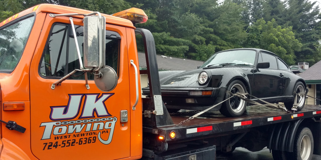 JK Towing's flatbed tow truck carrying an antique sports car that is carefully tied down with synthetic straps around its tires