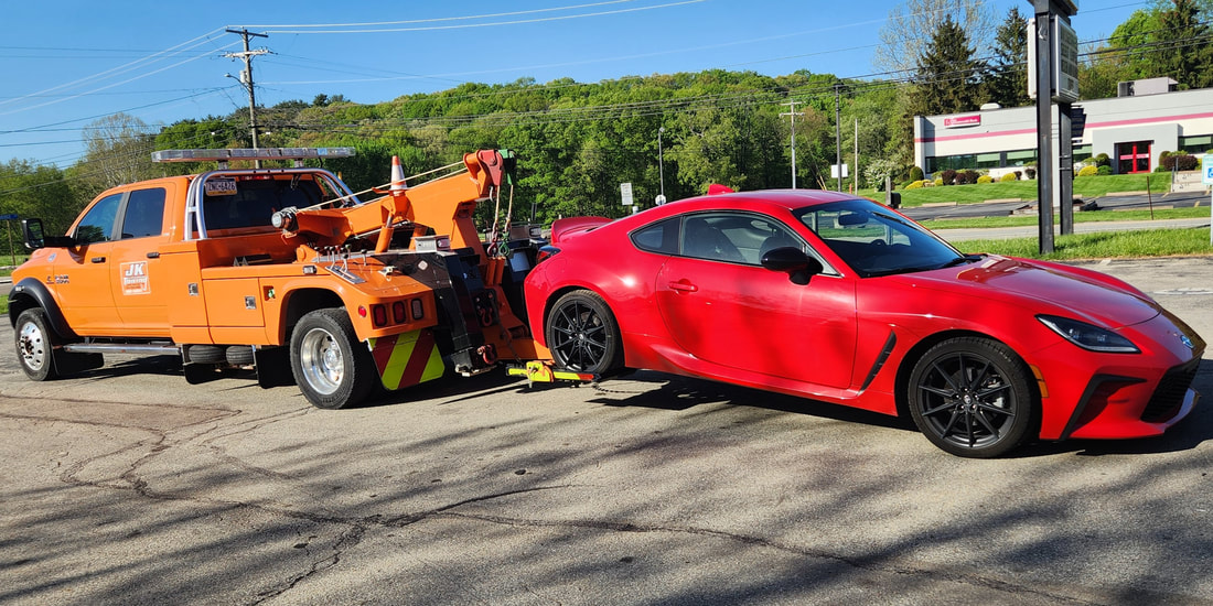 JK Towing's tow truck uses its wheel-lift boom to tow a sports car by its rear wheels
