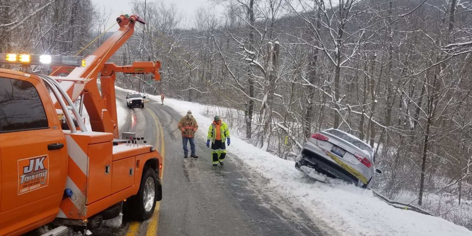 JK Towing's tow truck using its boom and winches to recover a car from a snow-covered embankment